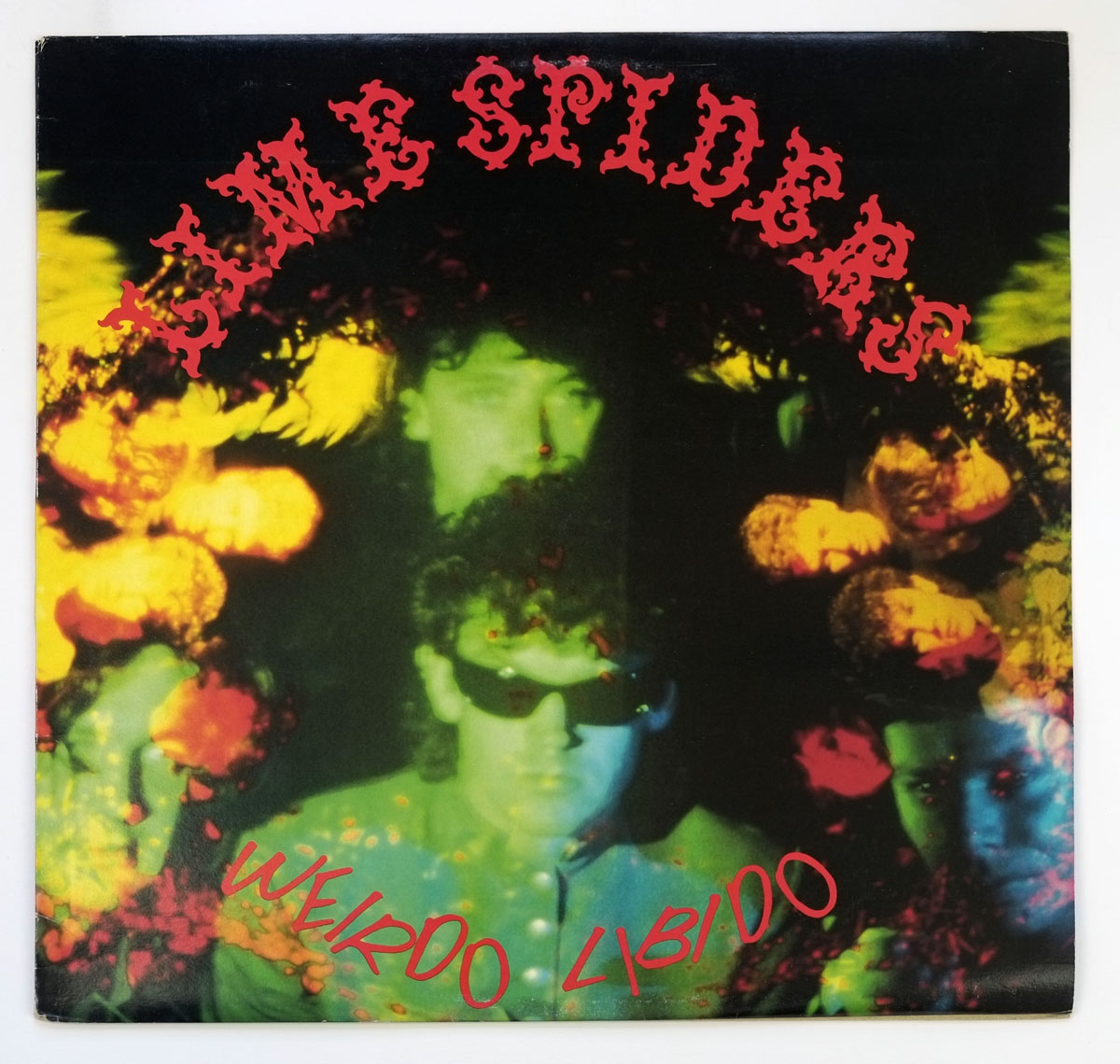 Album cover of Lime Spiders' 'Weirdo Libido' (1987). The cover features a surreal, psychedelic collage with a dark, neon-tinted photo of the band. The members' faces appear distorted and overlaid with vibrant green, red, and yellow hues, giving a ghostly, hallucinogenic effect. The band's name is in a jagged red font at the top, while the album title curves in red at the bottom.